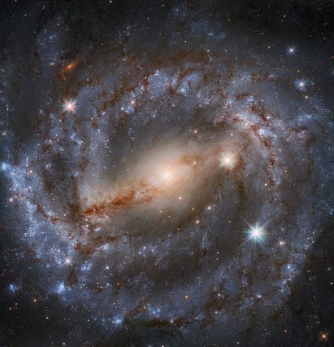 Hubble image of NGC 5643, a face-on spiral galaxy with a bright core, two main spiral arms laced with dark dust lanes, and pink star-forming regions.