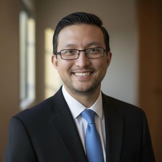 Aaron Beaudoin, smiling, in a dark suit and blue tie.
